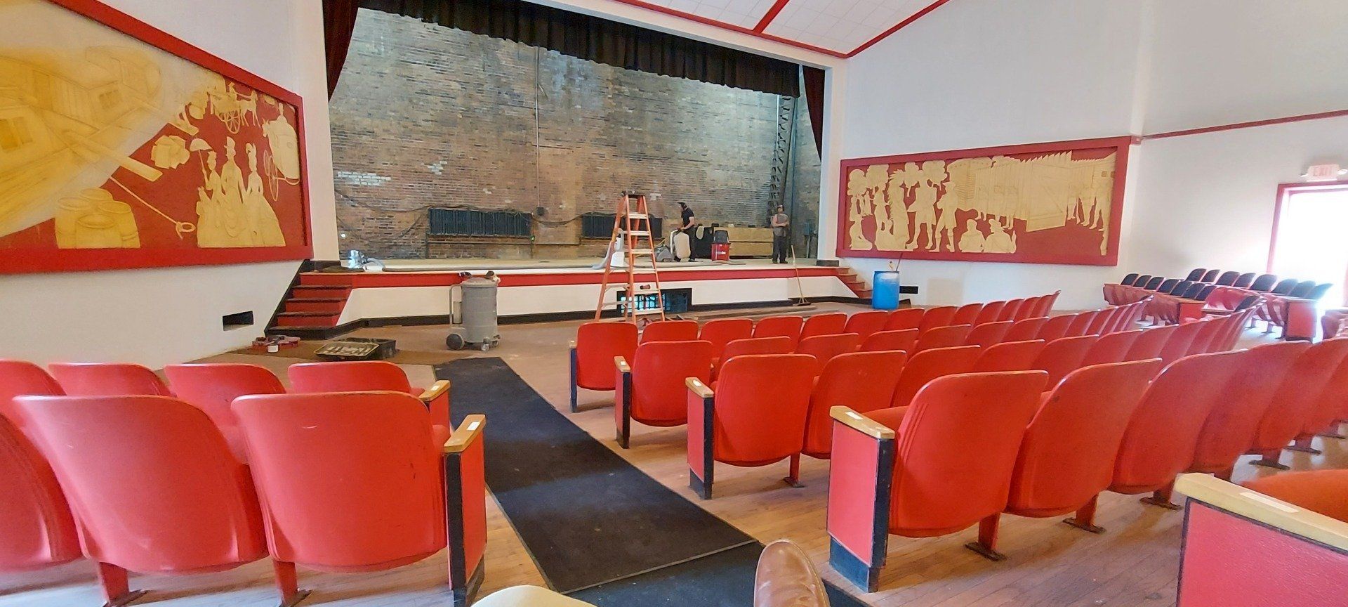 An empty auditorium with red seats and a stage.
