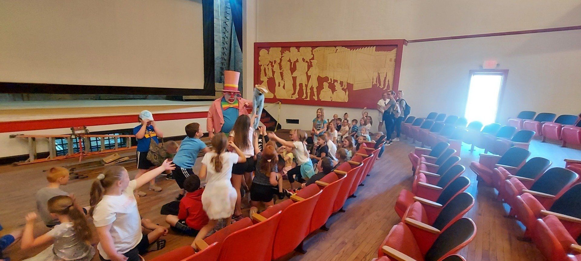 A group of children are sitting in an auditorium watching a clown.