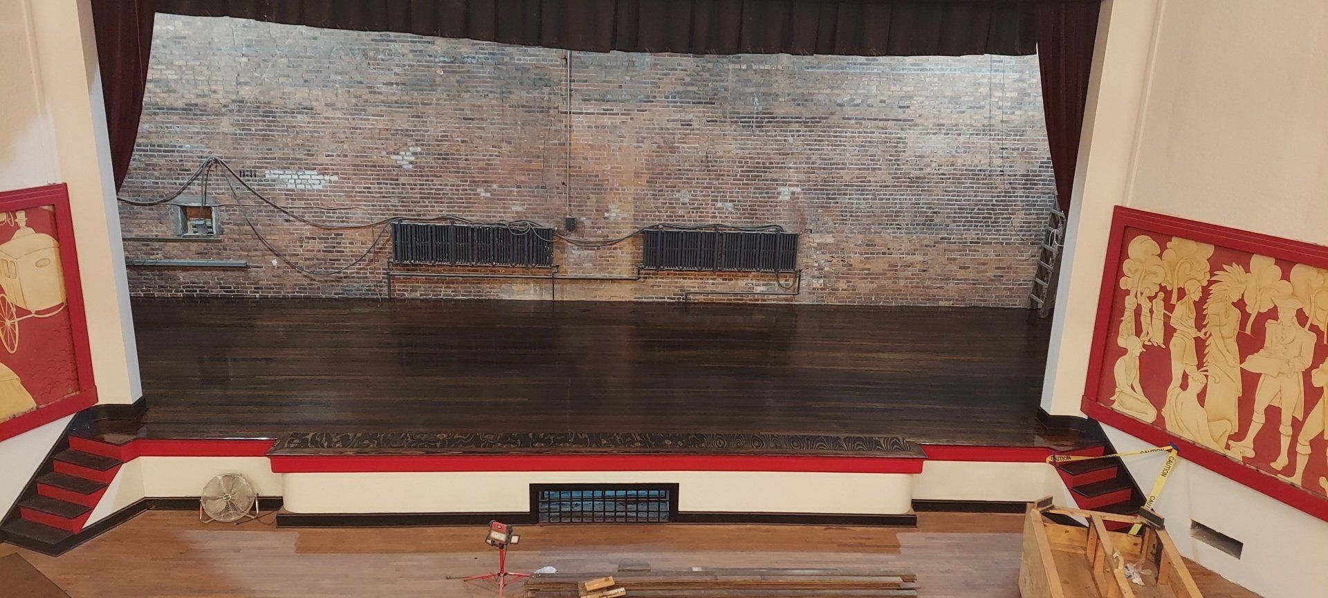 An empty stage in a theater with a red curtain and a brick wall.