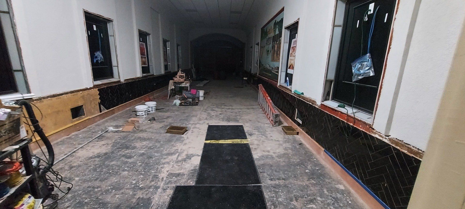 A long hallway with a black mat on the floor in a building under construction.