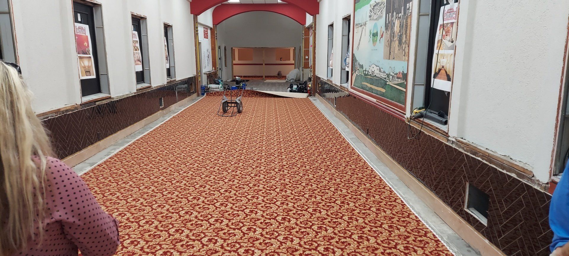 A woman is standing in a long hallway with a bowling alley in the background.