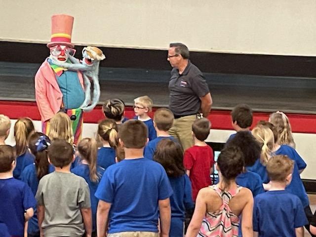 A group of children are standing in front of a clown wearing a top hat.