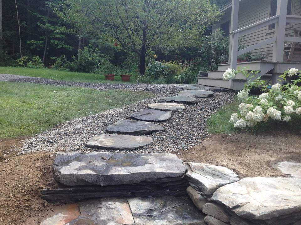 Stone path leading to a porch; flat, dark stones set in gravel alongside grass and a flower bed.