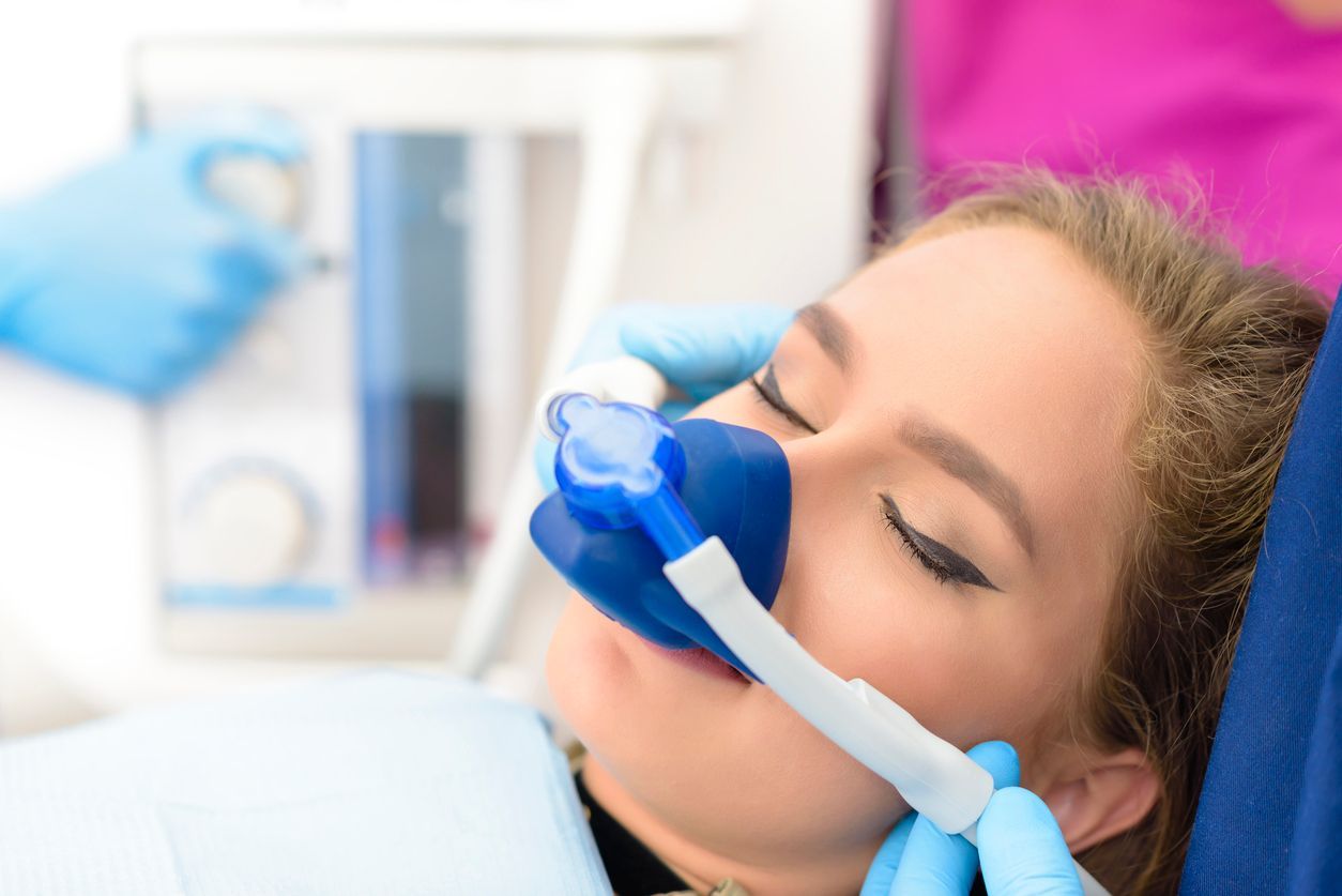 Woman receiving dental treatment with a blue oxygen mask; medical setting.