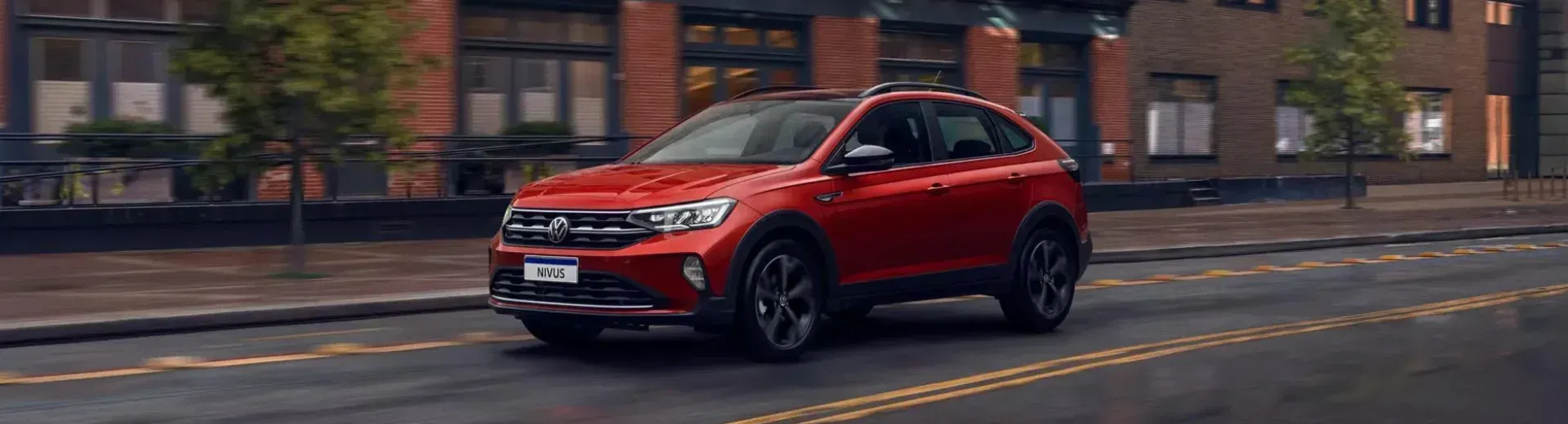 SUV vermelho trafegando em uma rua da cidade, com prédios ao fundo.