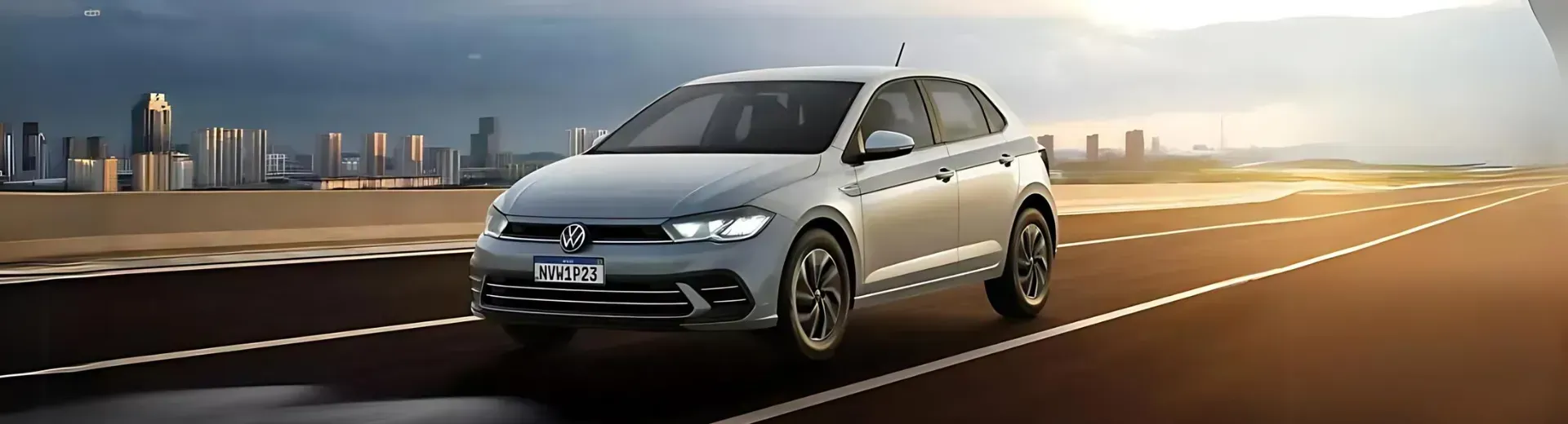 Um carro Volkswagen prateado trafega em uma rodovia com o horizonte da cidade ao fundo.
