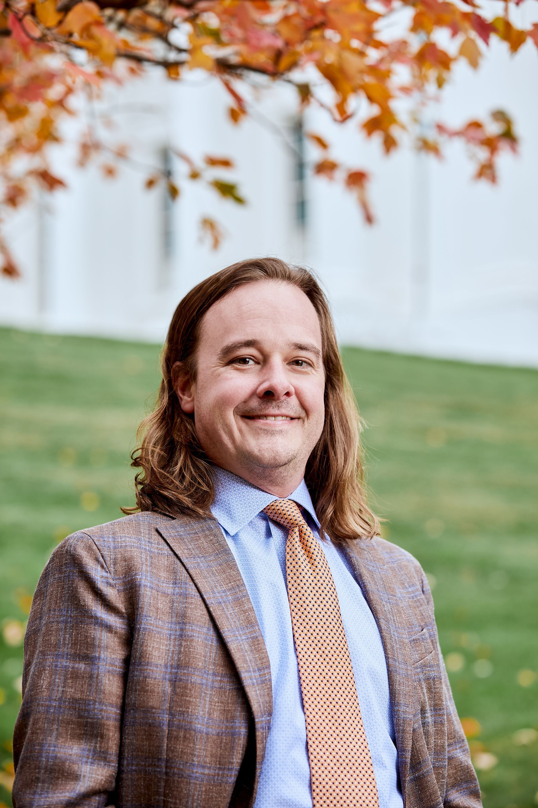 A man in a suit and tie is standing in front of a wooden wall.