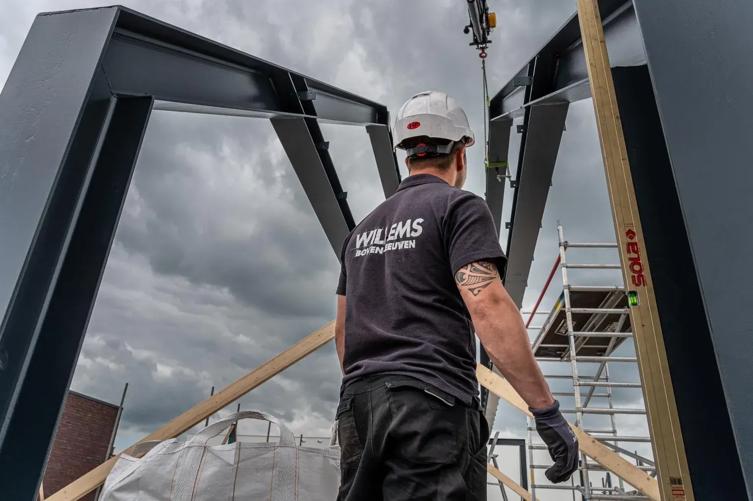 Een man met een harde hoed en een zwart shirt werkt aan een brug. Door Willems Boven-Leeuwen.