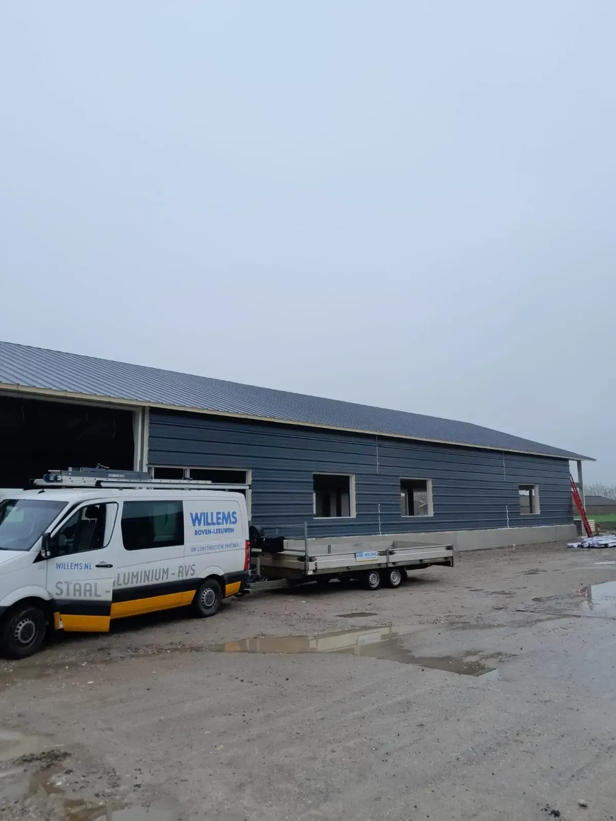 Een wit busje met het woord Wilson op de zijkant staat geparkeerd voor een gebouw in aanbouw
