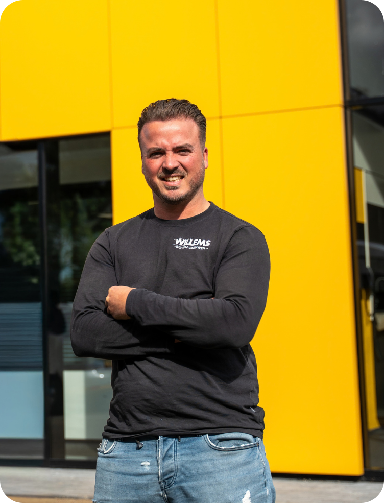 Een jonge man in een groen jasje en spijkerbroek staat in een fabriek. Bas Lamers