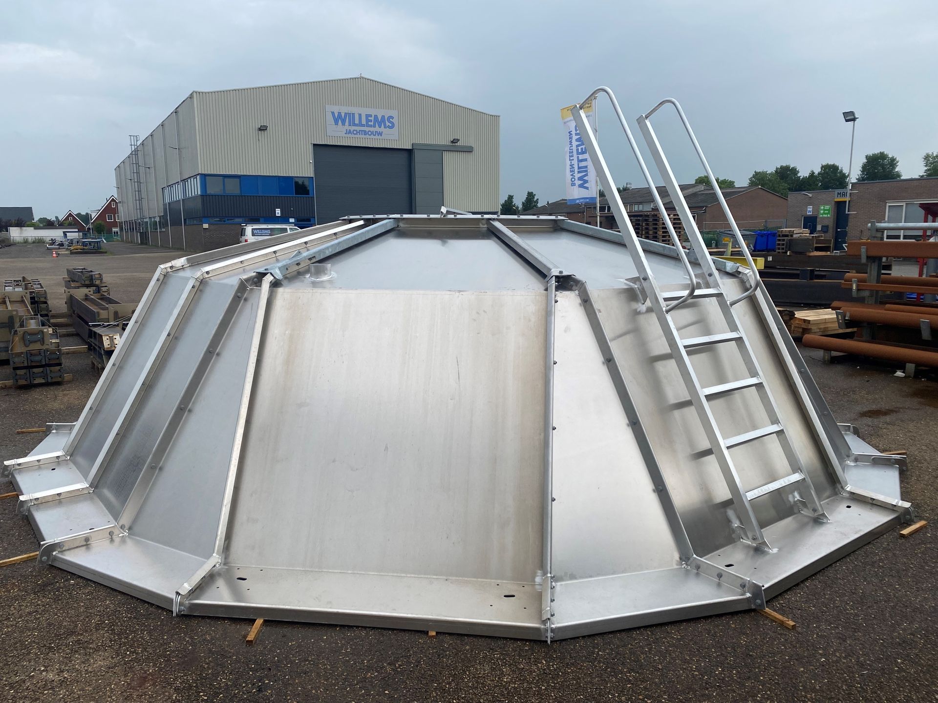Een grote, metalen, meerzijdige industriële afdekking of tankdak met een aangehechte ladder, gelegen op een buitenterrein.