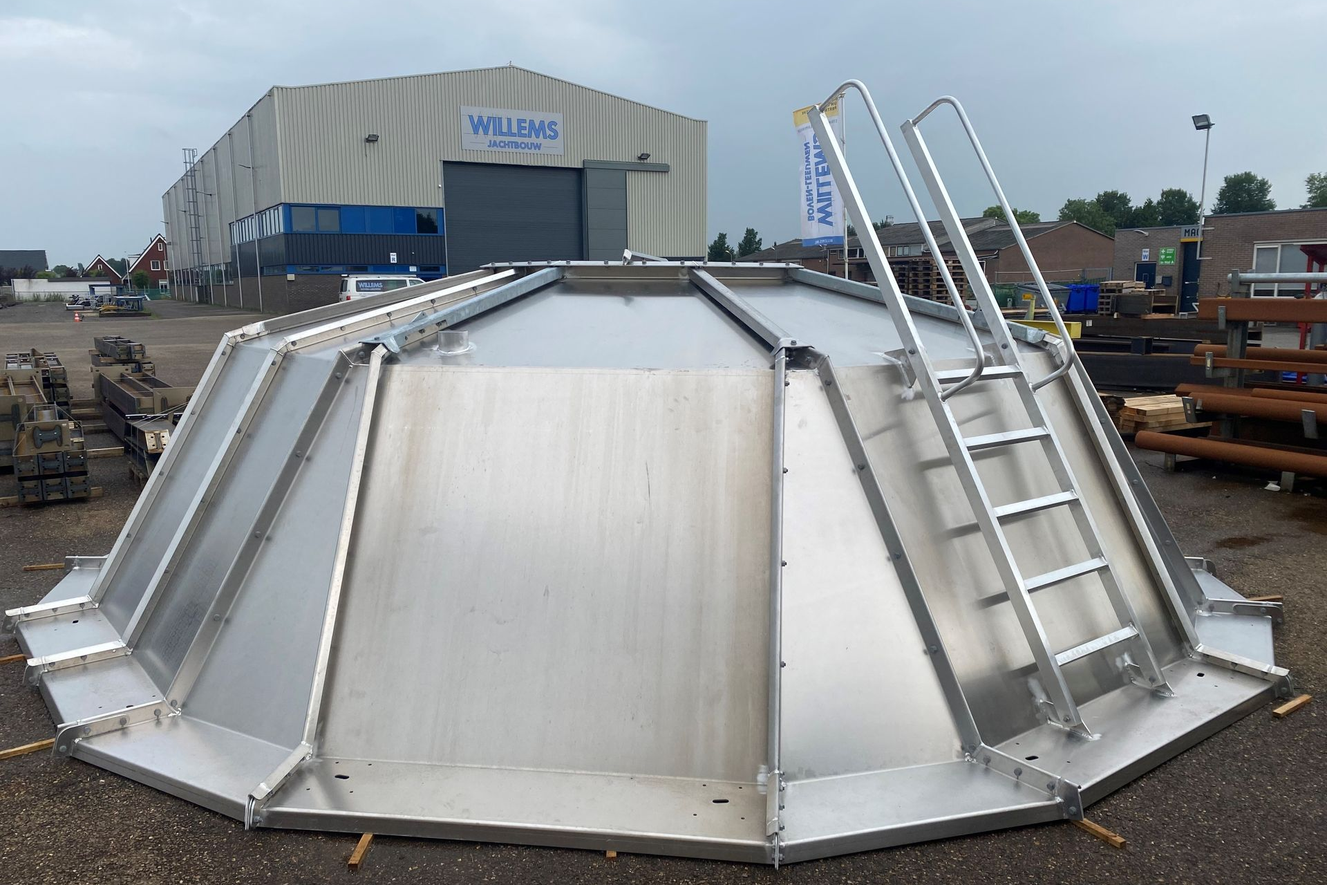 Een grote, zilverkleurige, veelzijdige metalen tankafdekking met een aangehechte toegangsladder, gelegen op een industrieterrein in de openlucht.