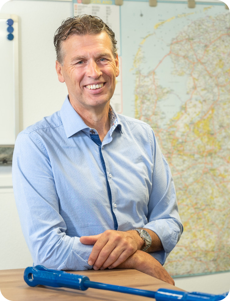 Een man in een blauw shirt zit met zijn armen over elkaar aan een tafel. Marcel Hol.