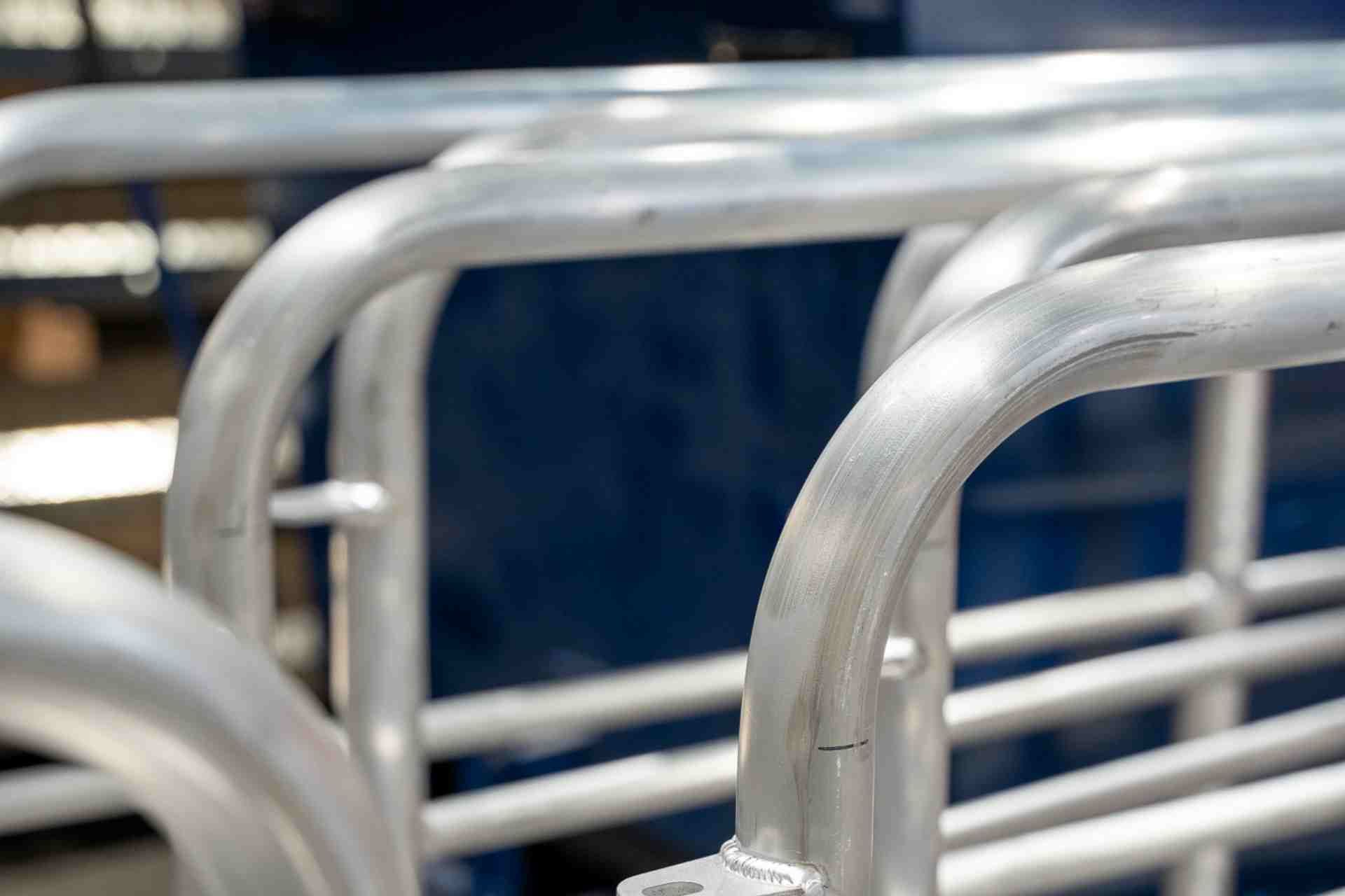 Detailopname van meerdere gebogen, geborstelde metalen buizen die samen een opslagrek of veepoort vormen.
