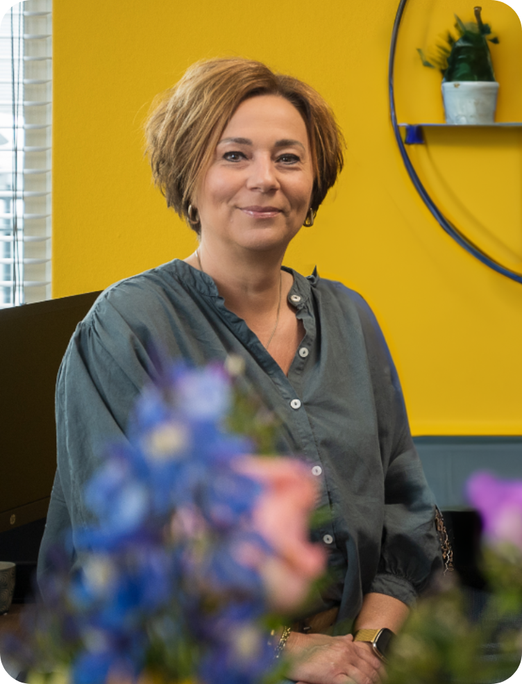 Een vrouw in een shirt met luipaardprint glimlacht voor een gele muur. Ramona Meijer