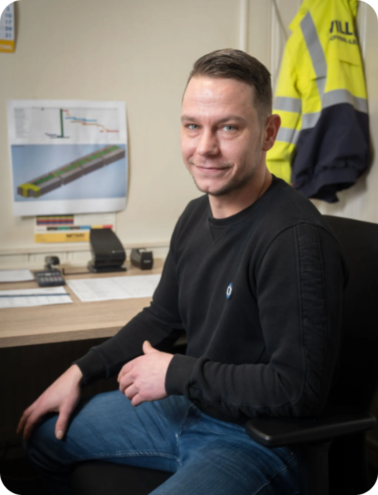 Een man, gekleed in een zwart shirt en een geel jasje, zit aan een bureau. Harm van Dinteren.