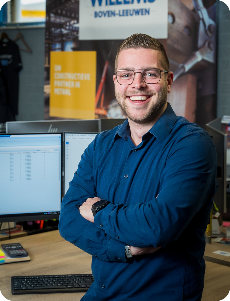 Een jonge man in een groen jasje en spijkerbroek staat in een fabriek. Bas Lamers