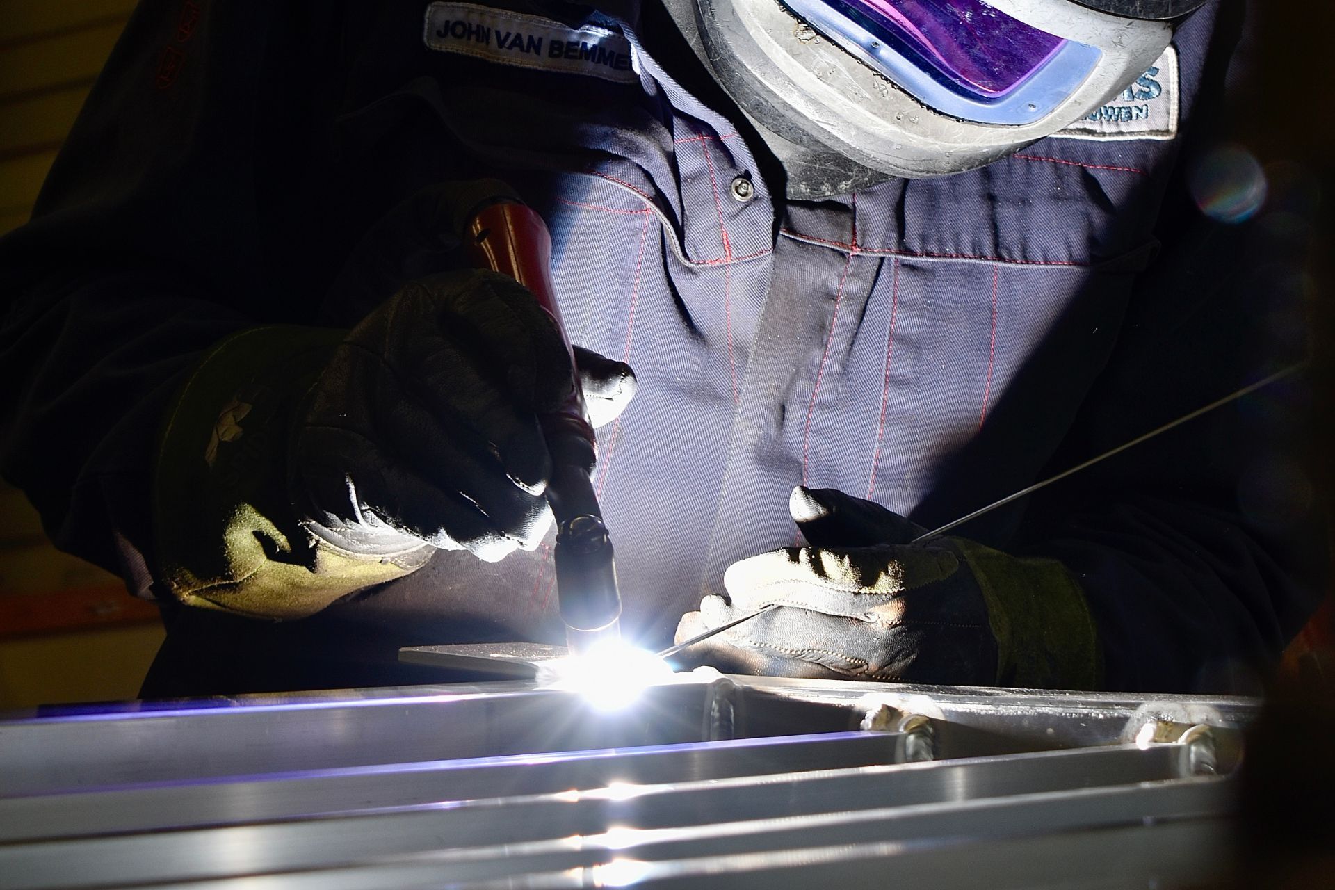 Een lasser, die een beschermend masker en handschoenen draagt, voert nauwkeurig metaallassen uit, waarbij een heldere boog op een metalen oppervlak ontstaat.