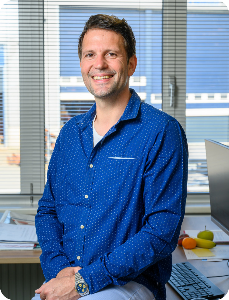 Een man in een blauw shirt zit aan een bureau voor een raam. Marcel van Rotterdam