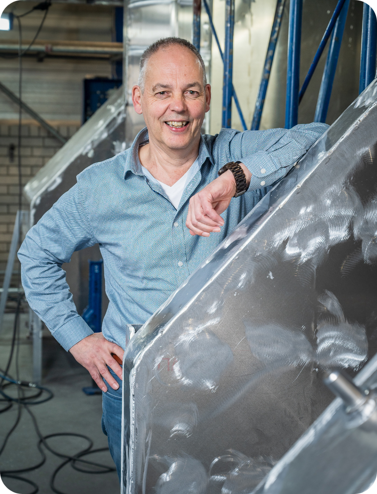 Een man in een blauw shirt en spijkerbroek zit op een trap. Hans van den Berk.