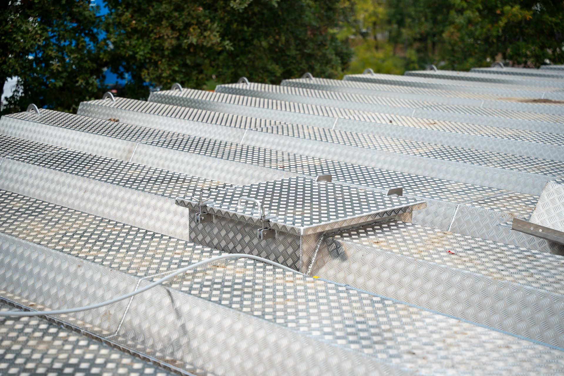 Een grote, zilverkleurige, veelzijdige metalen tankafdekking met een aangehechte toegangsladder, gelegen op een industrieterrein in de openlucht.