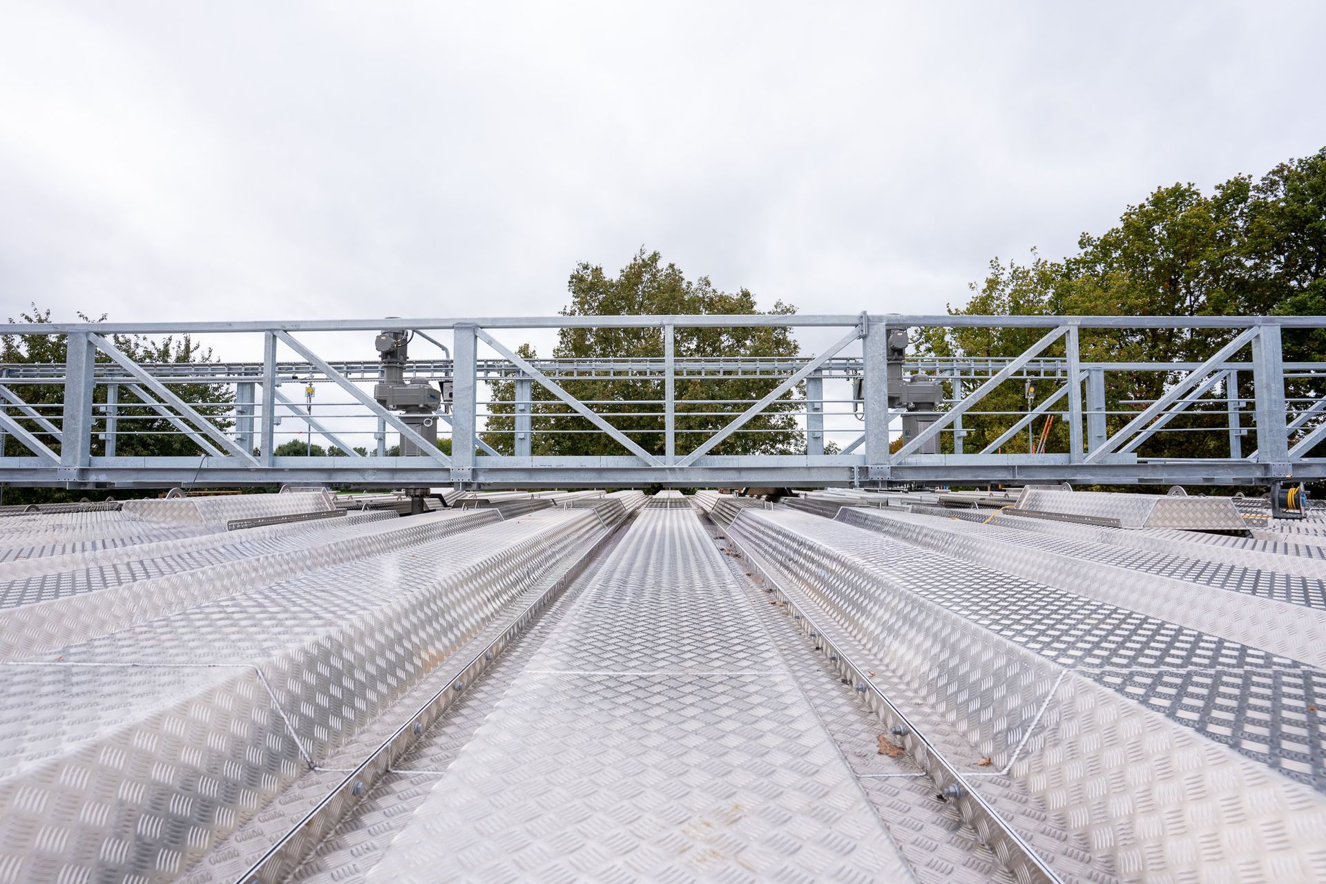 Een groot, metalen, veelzijdig cirkelvormig afdek- of dakelement dat op een grindterrein staat onder een bewolkte hemel.