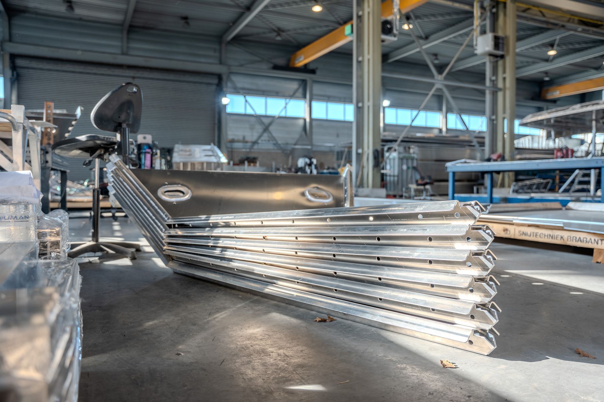 Een stapel gebogen, metalen industriële panelen in een helder verlichte, ruime werkplaats of productiehal.
