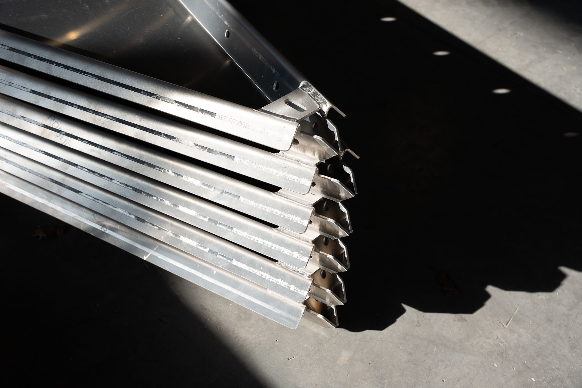 Een stapel van meerdere parallelle, geperforeerde metalen stroken die onder een hoek zijn uitgelijnd tegen een donkere achtergrond.