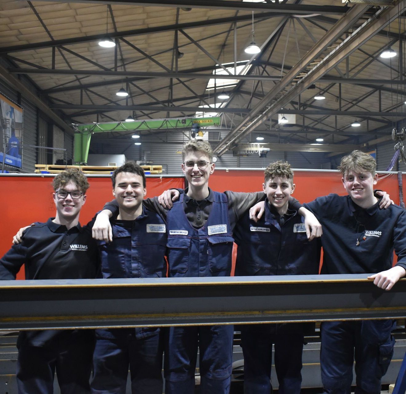 Een groep jonge mannen poseert voor een foto in een fabriek Door Willems Boven-Leeuwen.