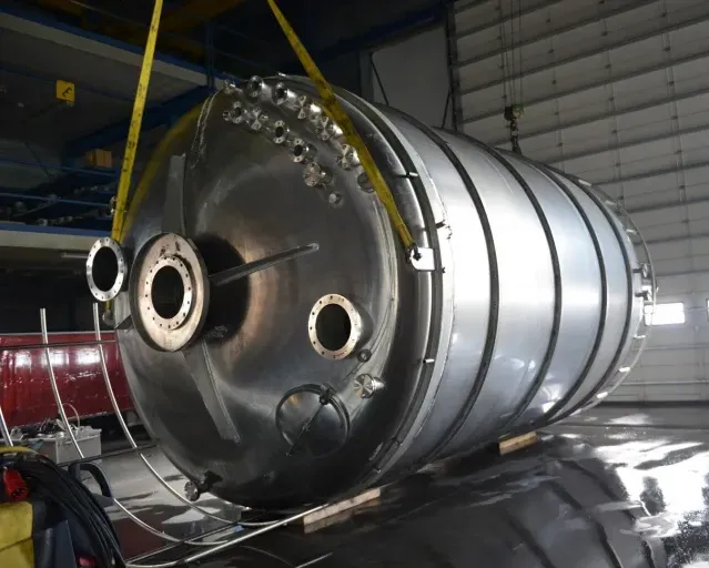 Een grote roestvrijstalen tank wordt door een kraan opgetild