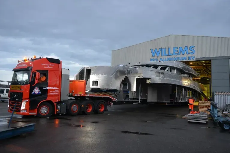 Een grote vrachtwagen vervoert een boot een gebouw binnen.
