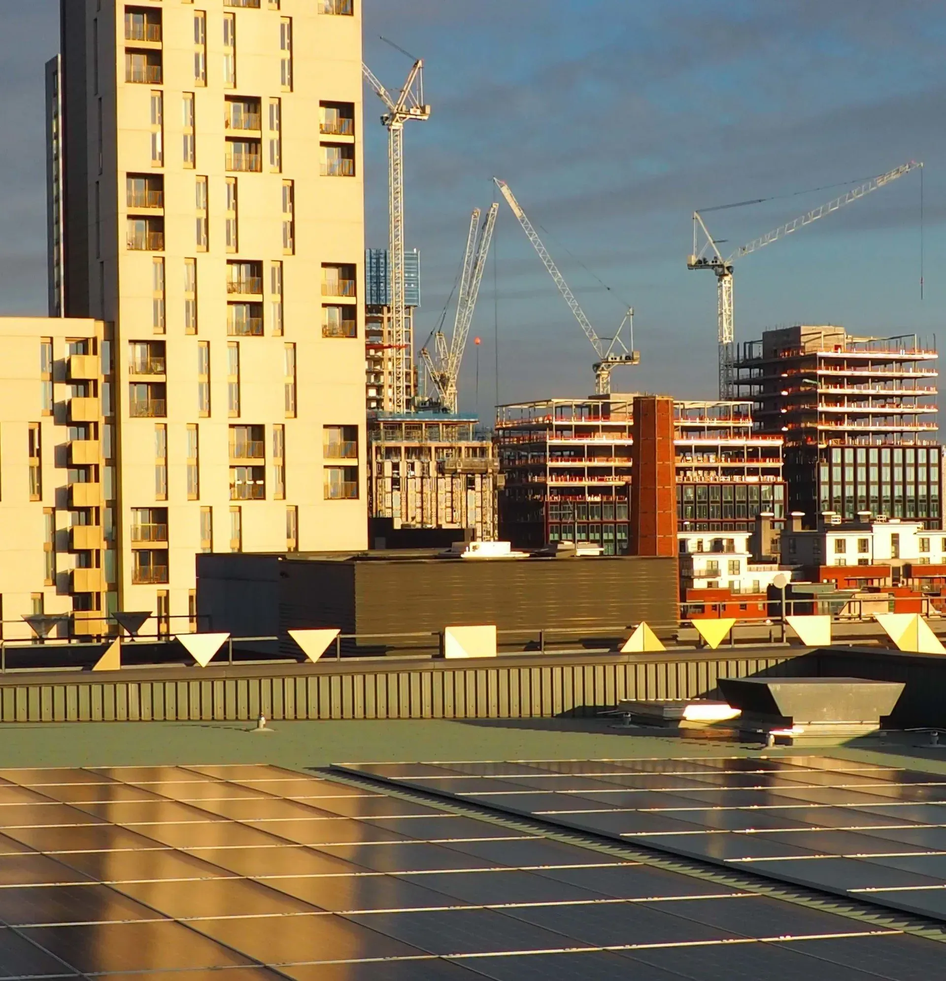 Skyscrapers and construction cranes in a city with solar panels in the foreground.