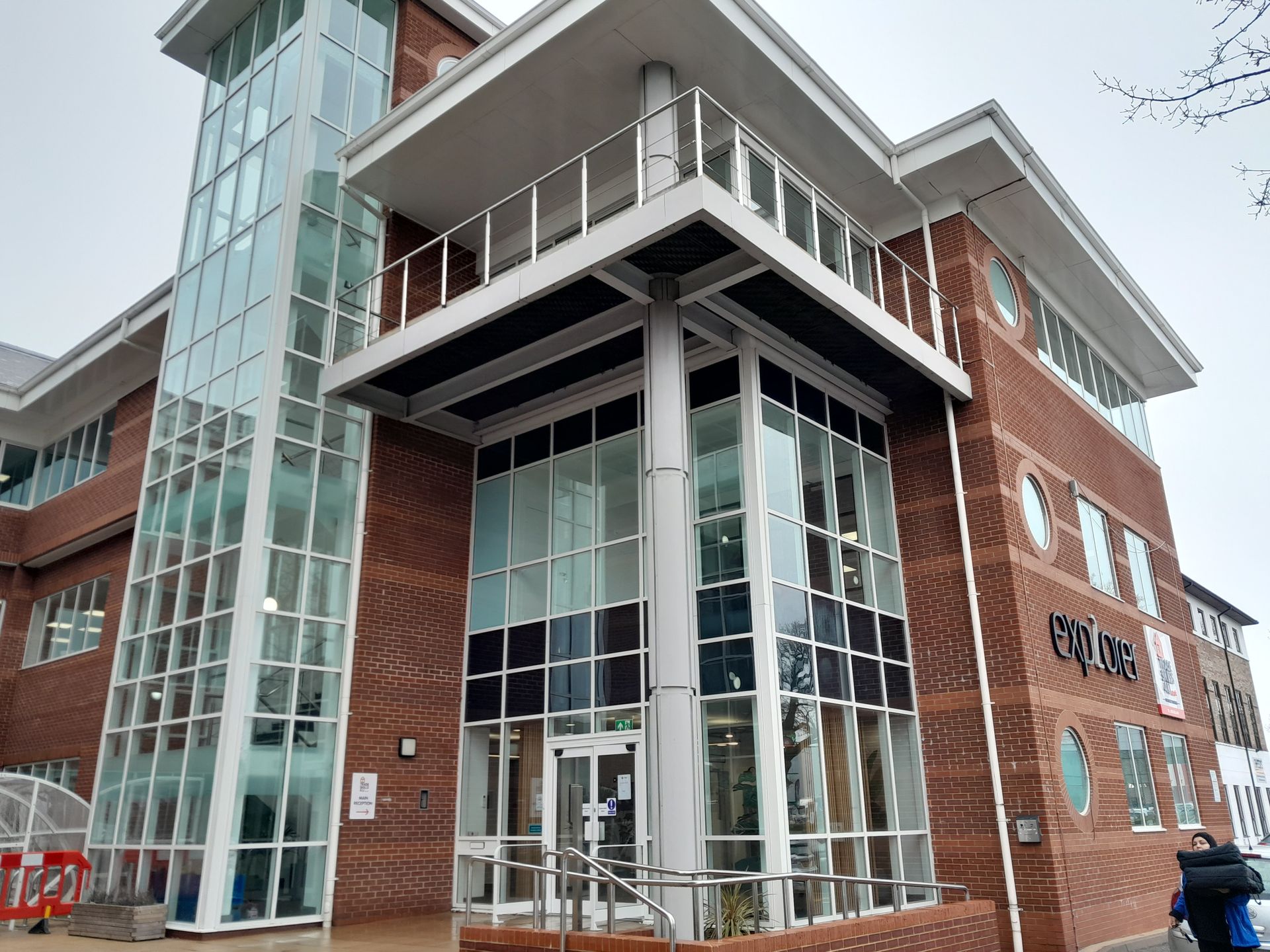 Modern brick office building with glass facade, balcony, and elevator tower.