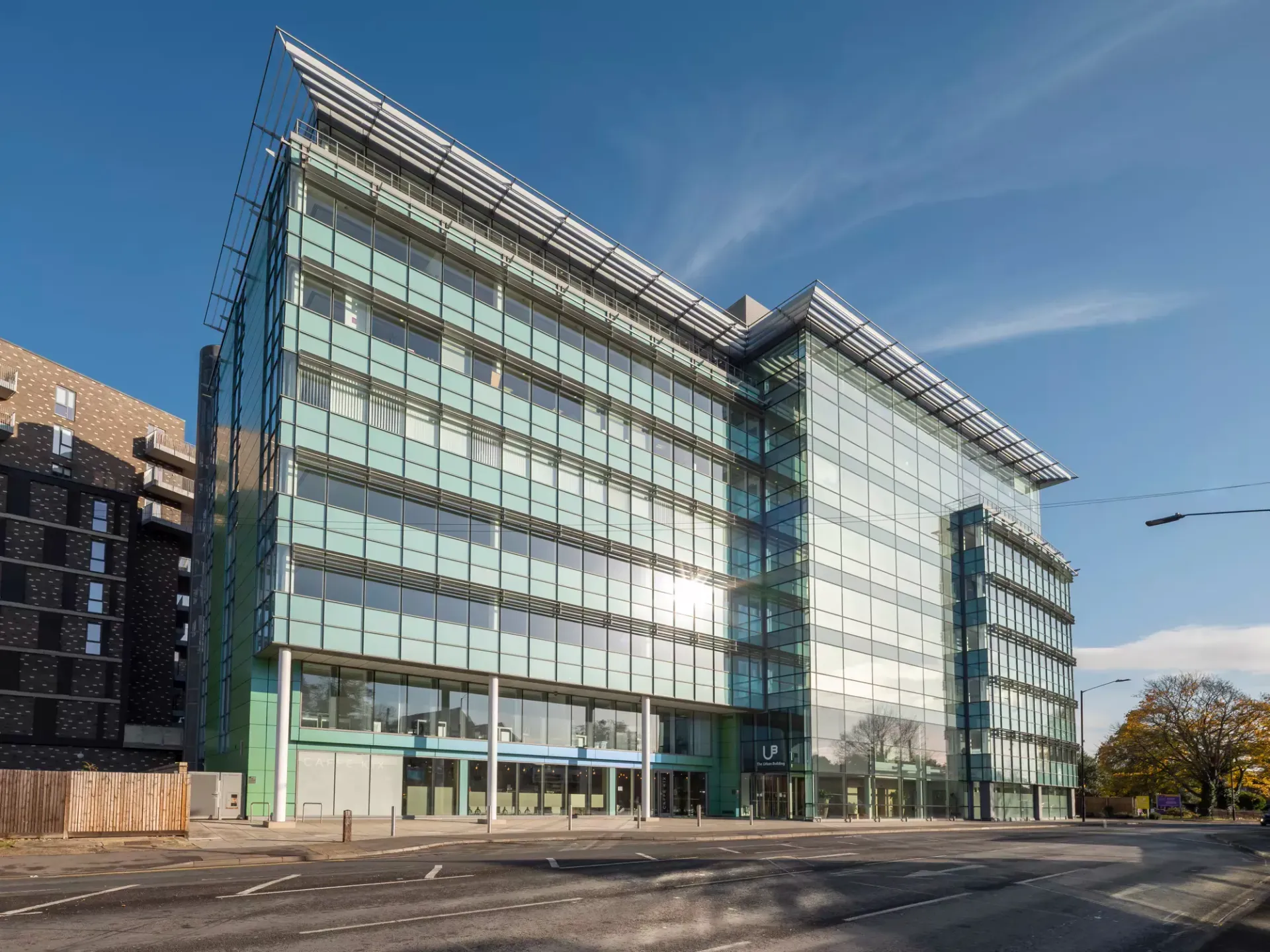 Large glass and steel office building shining in the sun, with an empty road in the forefront. 