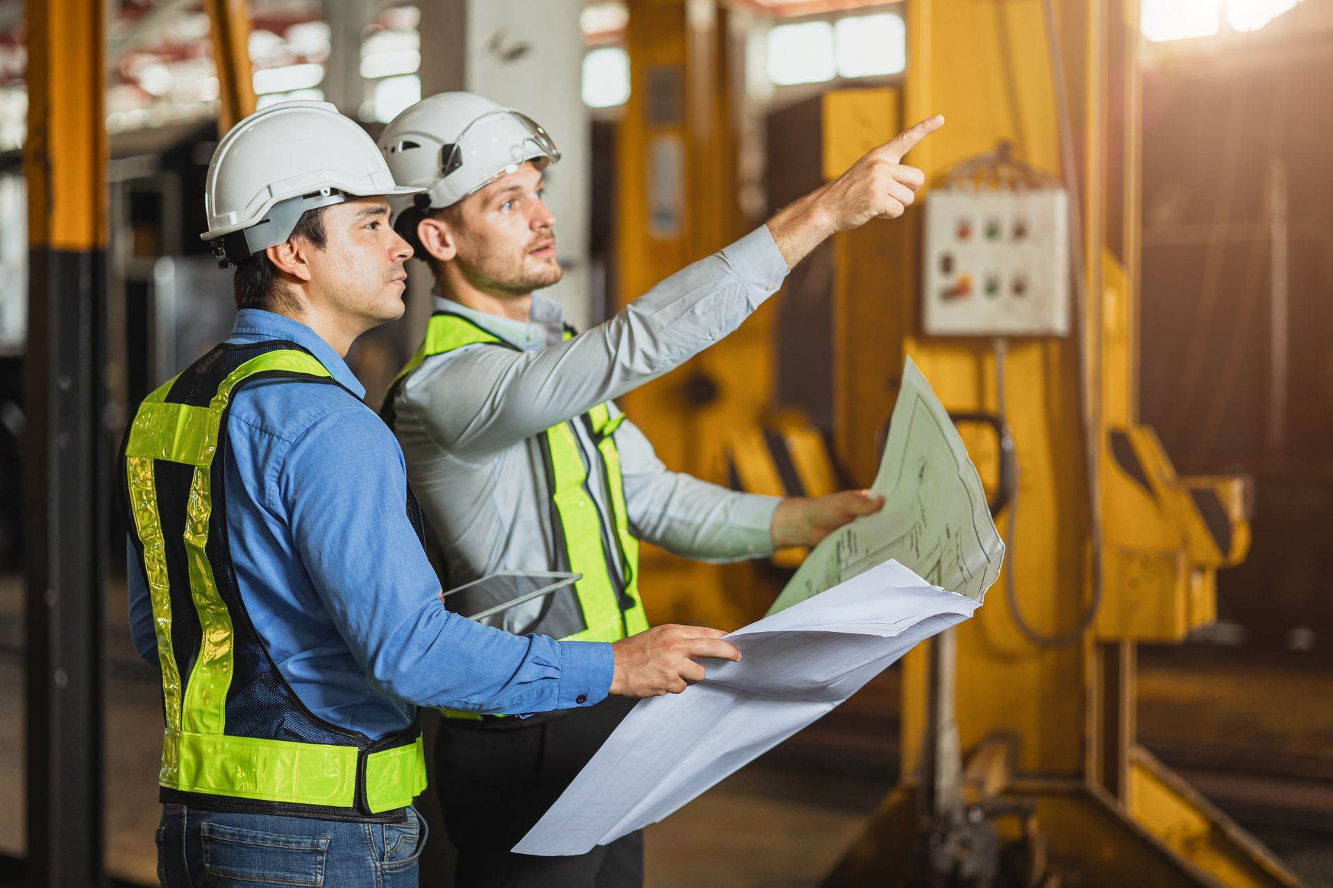 two men wearing hard hats and safety vests are looking at a blueprint