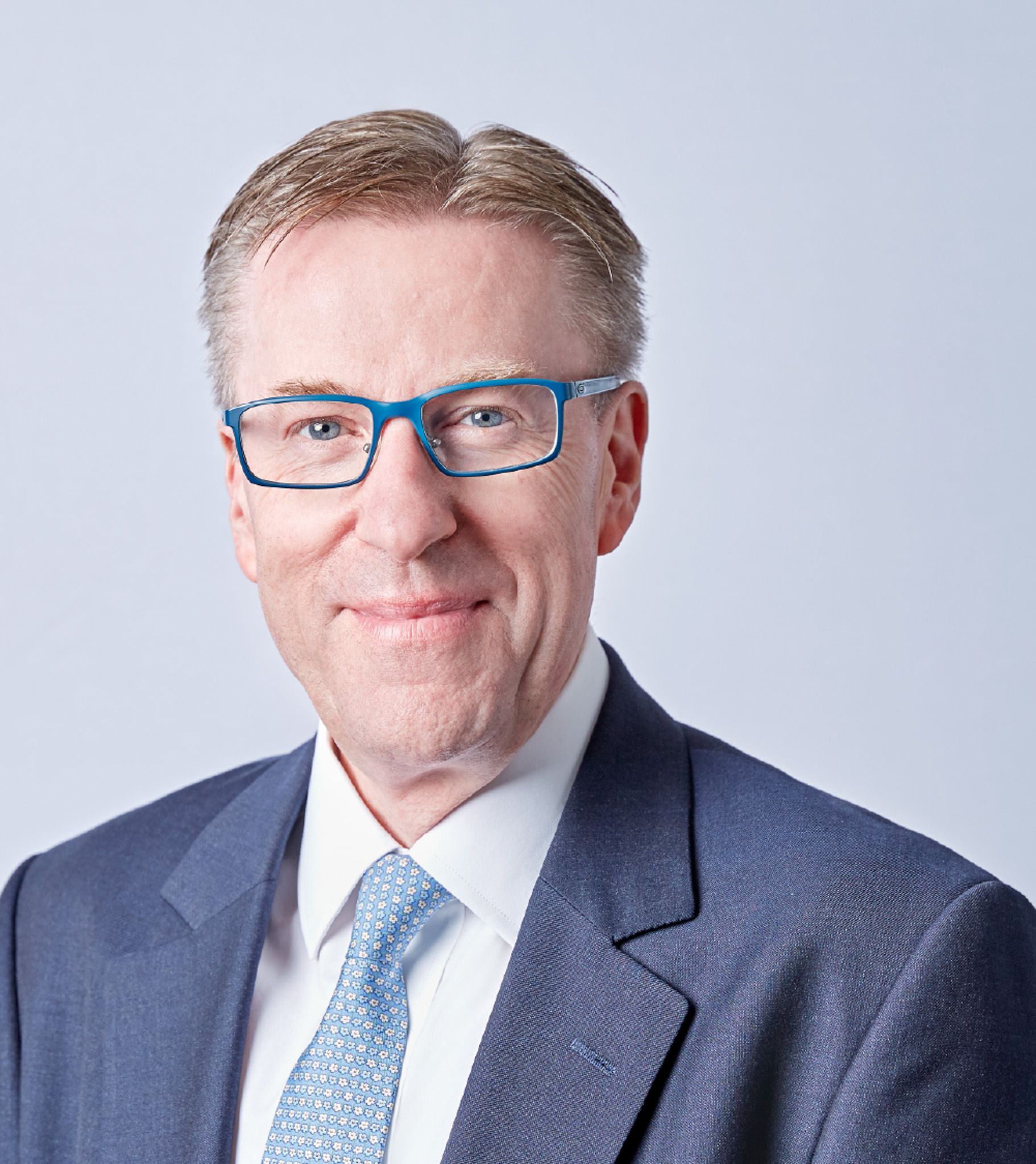 Man in blue suit, glasses, smiling, studio shot.
