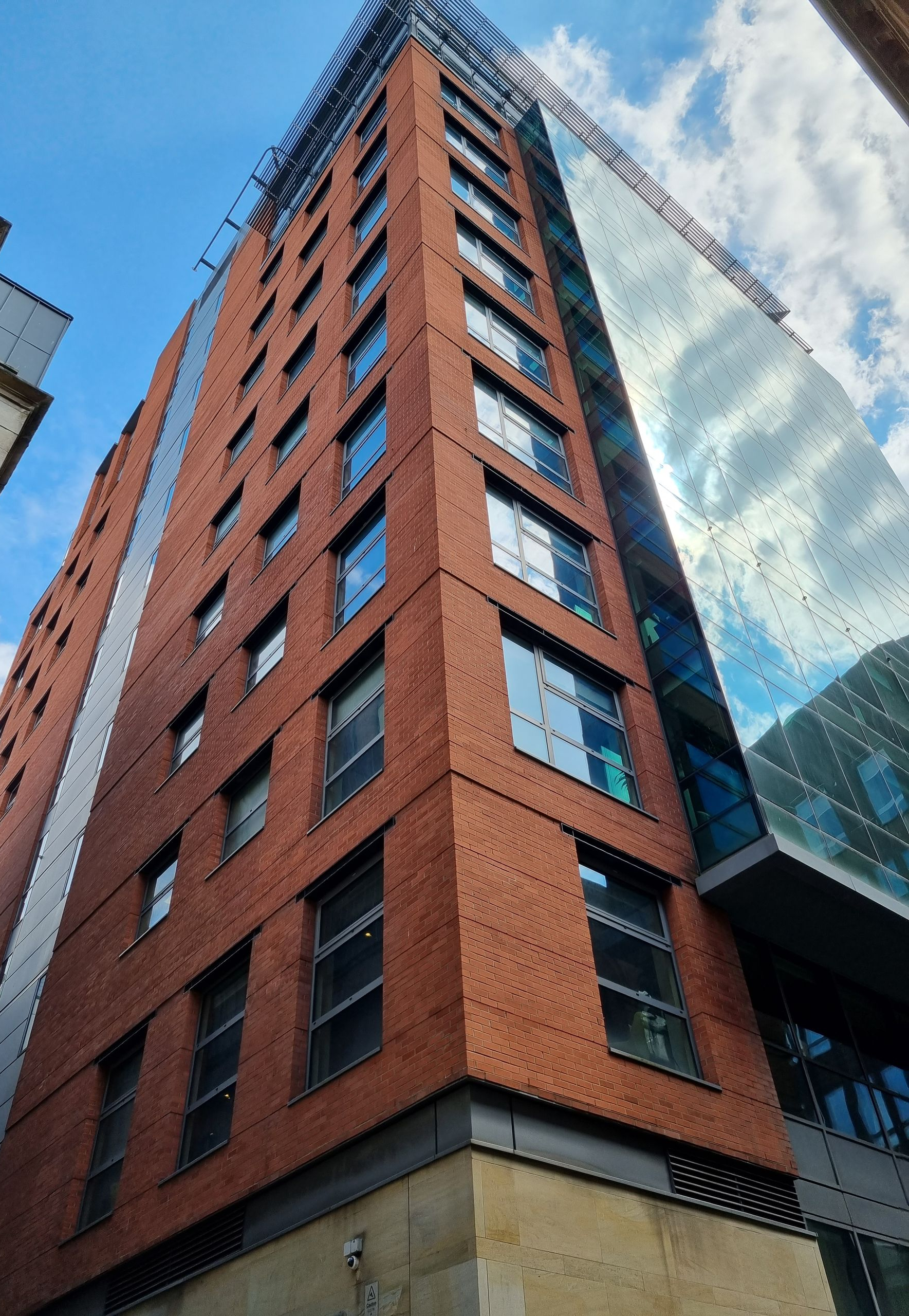 Tall brick and glass high-rise building against a blue sky, viewed from a low angle.