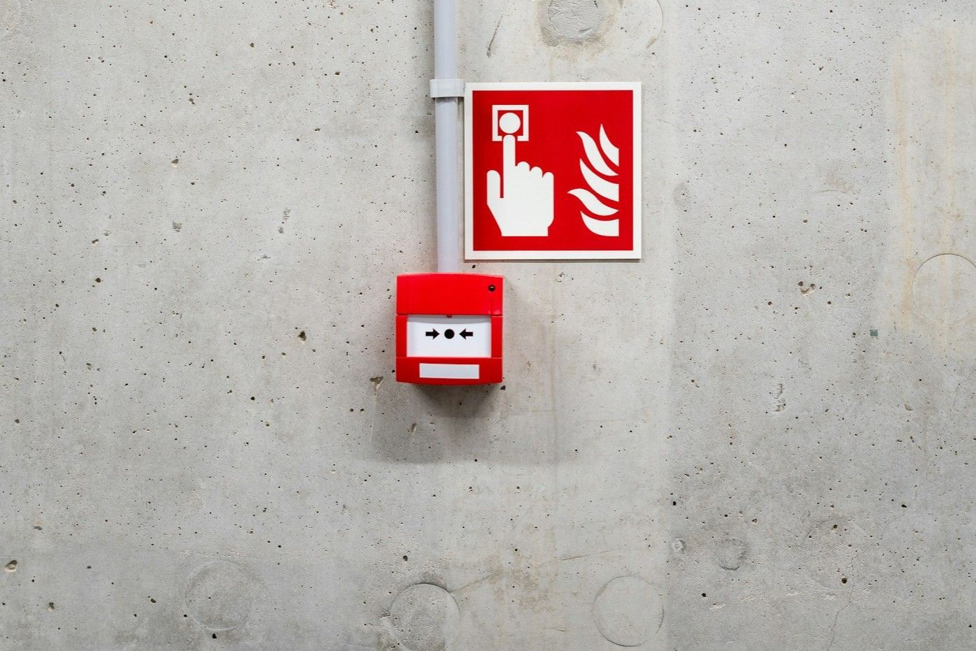Red fire alarm box and sign mounted on a concrete wall.