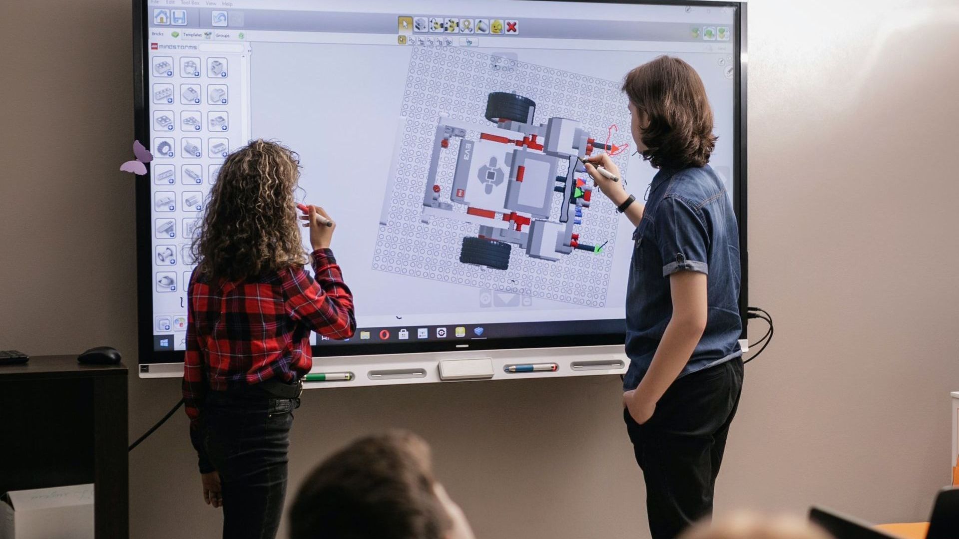 Two people point at a digital engineering plan on a large screen in a bright room.