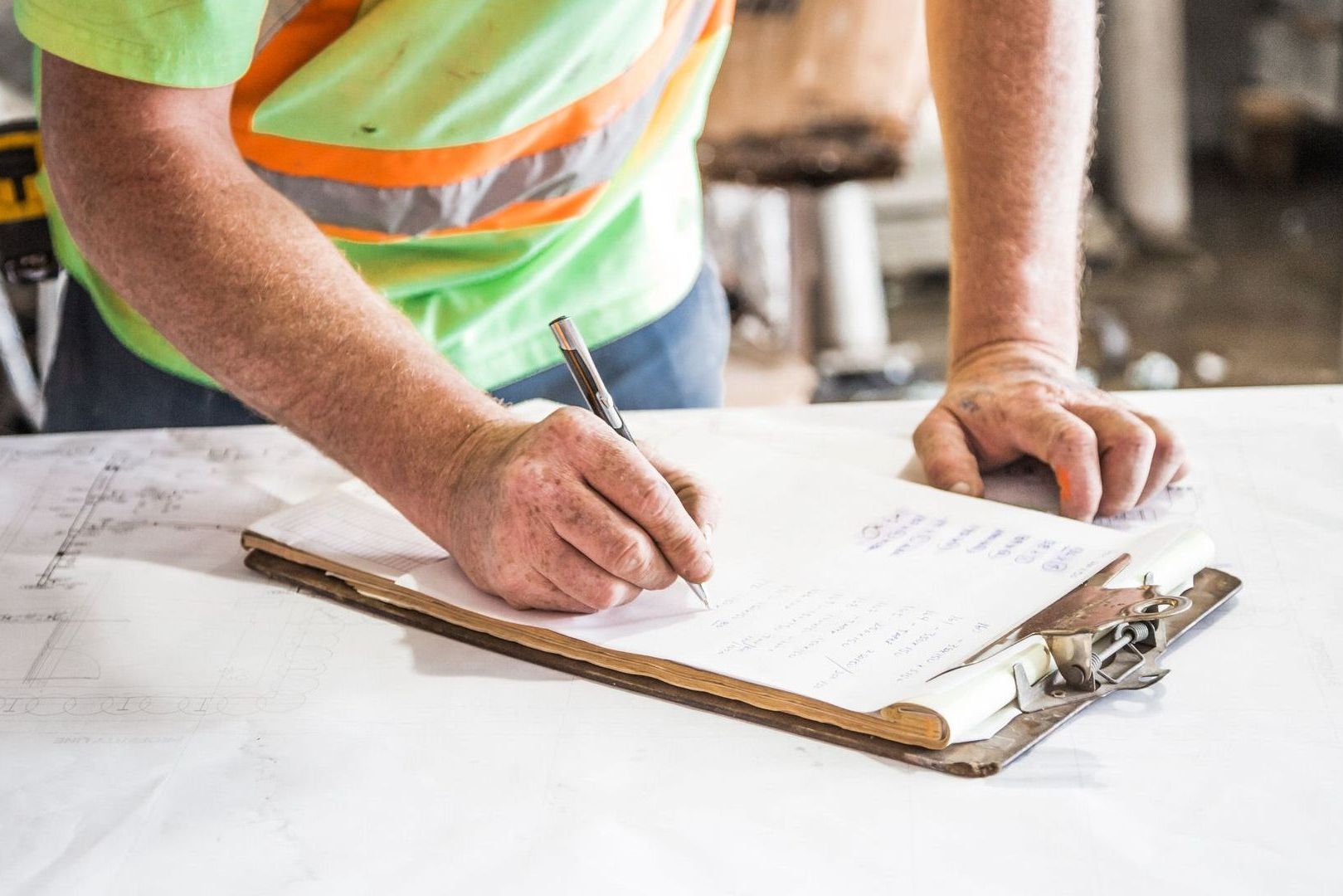 Person in reflective vest writing on clipboard, possibly at a construction site.