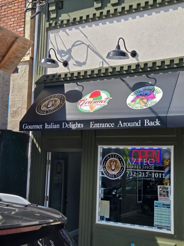 Exterior of an ice cream shop with black awning, lights, and signs. Says 