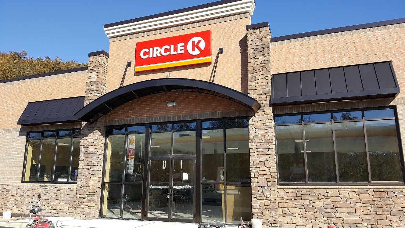 Circle K convenience store with stone facade, glass windows, and black awning under a blue sky.