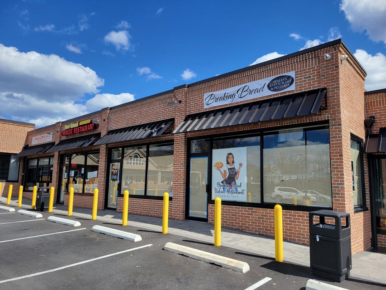 A strip mall with brick facades, black awnings, and a blue sky. Businesses include restaurants with signage.