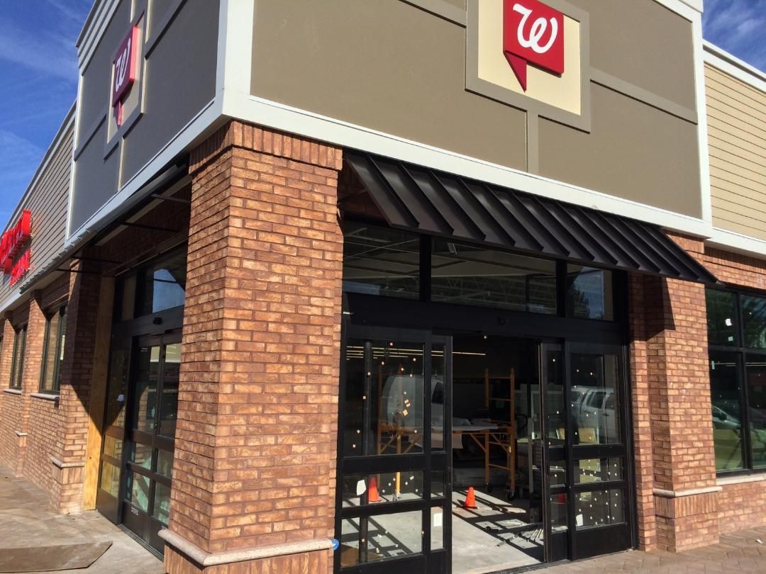 Walgreens store entrance with brick columns, glass doors, and awning. The building has a tan and gray facade.