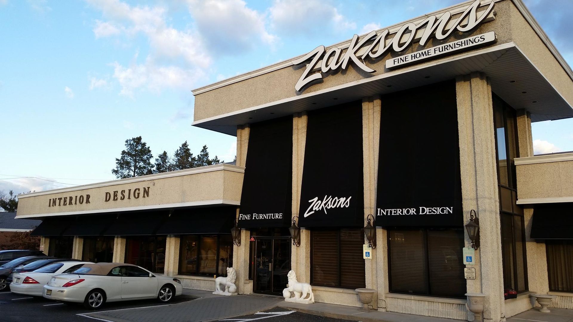 Zukson's Interior Design storefront with black awnings, beige facade, and parked cars.