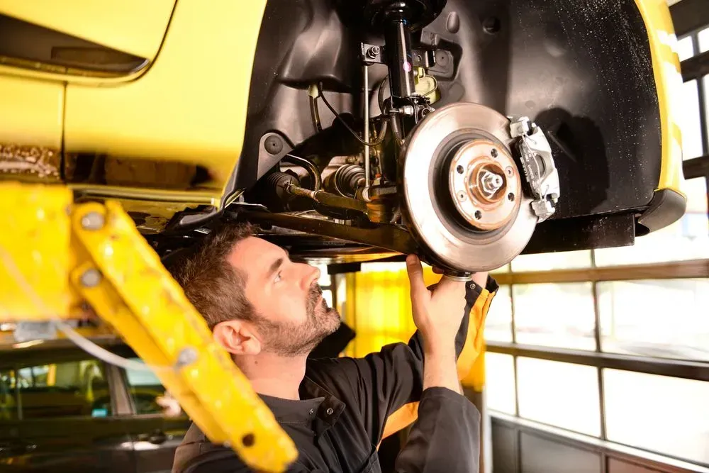 Mechanic Inspecting Car Brakes, Working Under a Yellow Car on a Lift  — B Wild Auto Repairs In North Gosford, NSW