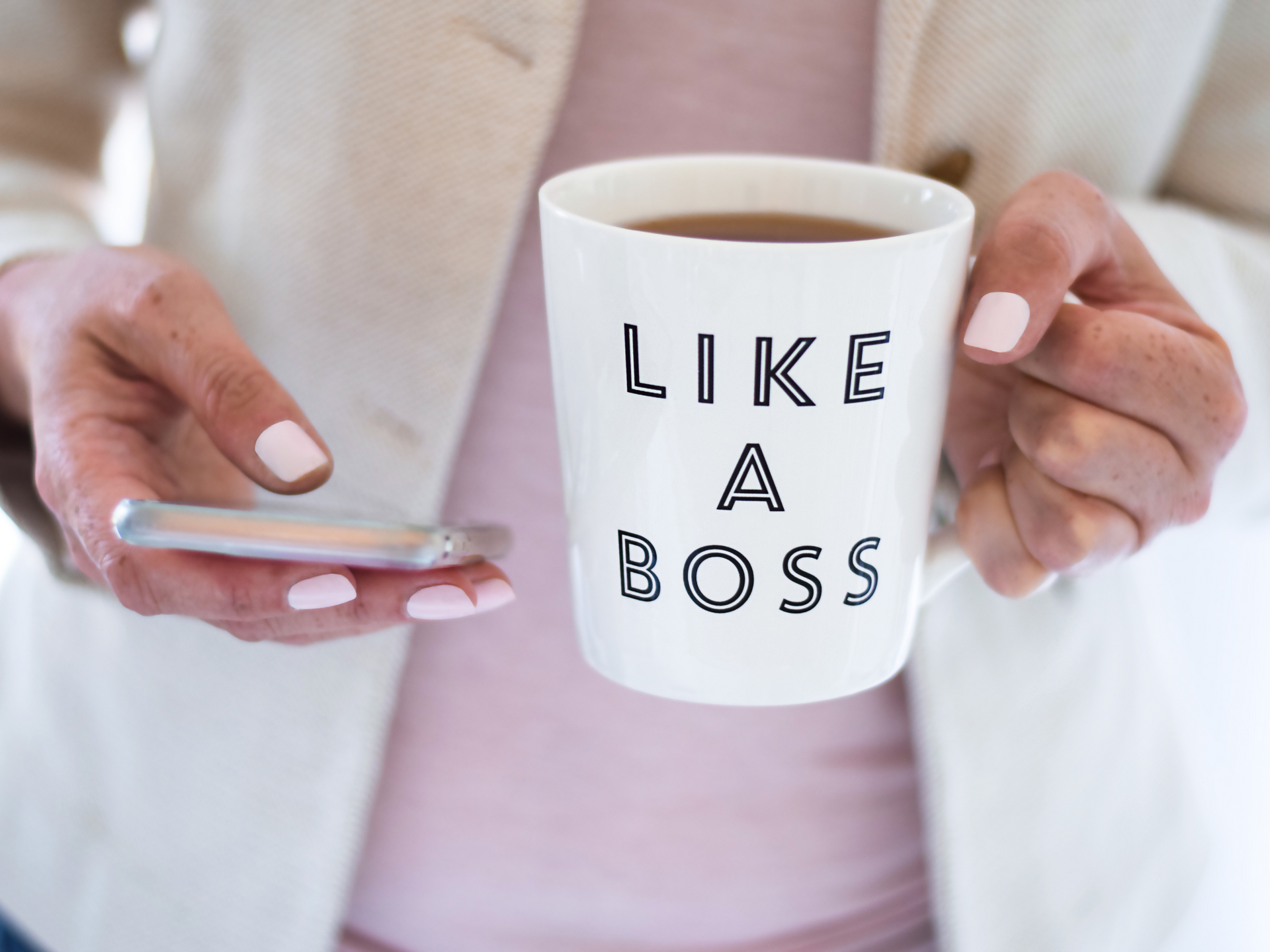 A woman is holding a cup of coffee and a cell phone.