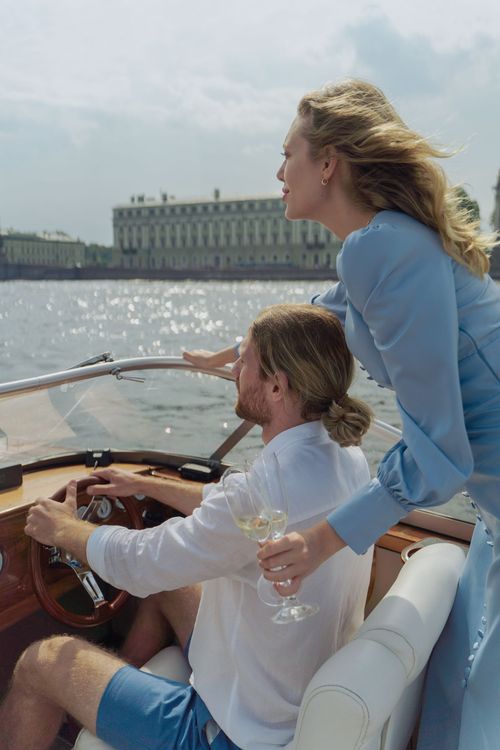 Two people on a boat on sparkling water, with a large building in the distance.
