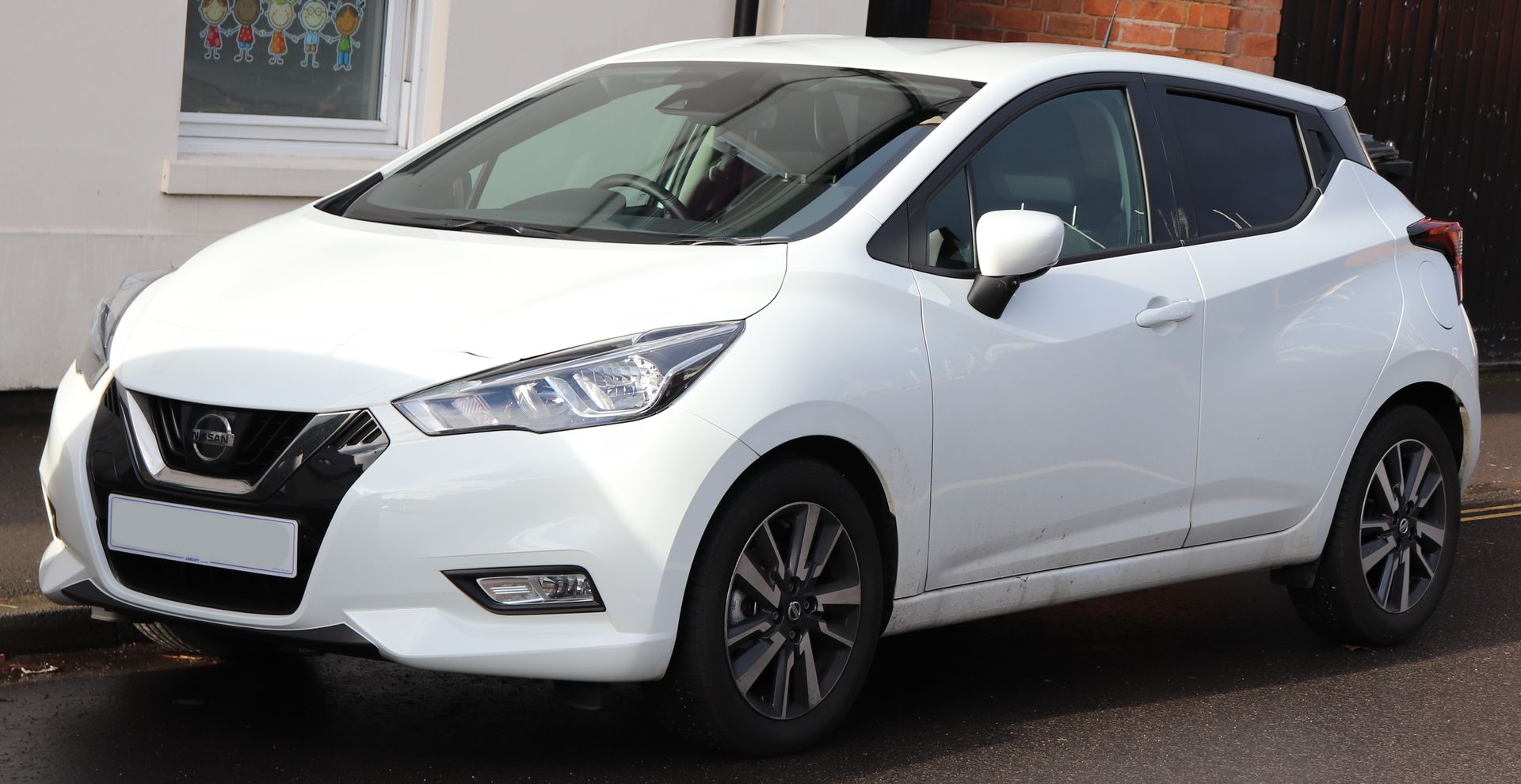 A white nissan micra hatchback is parked on the side of the road.