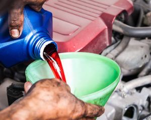 A person is pouring oil into a green funnel.